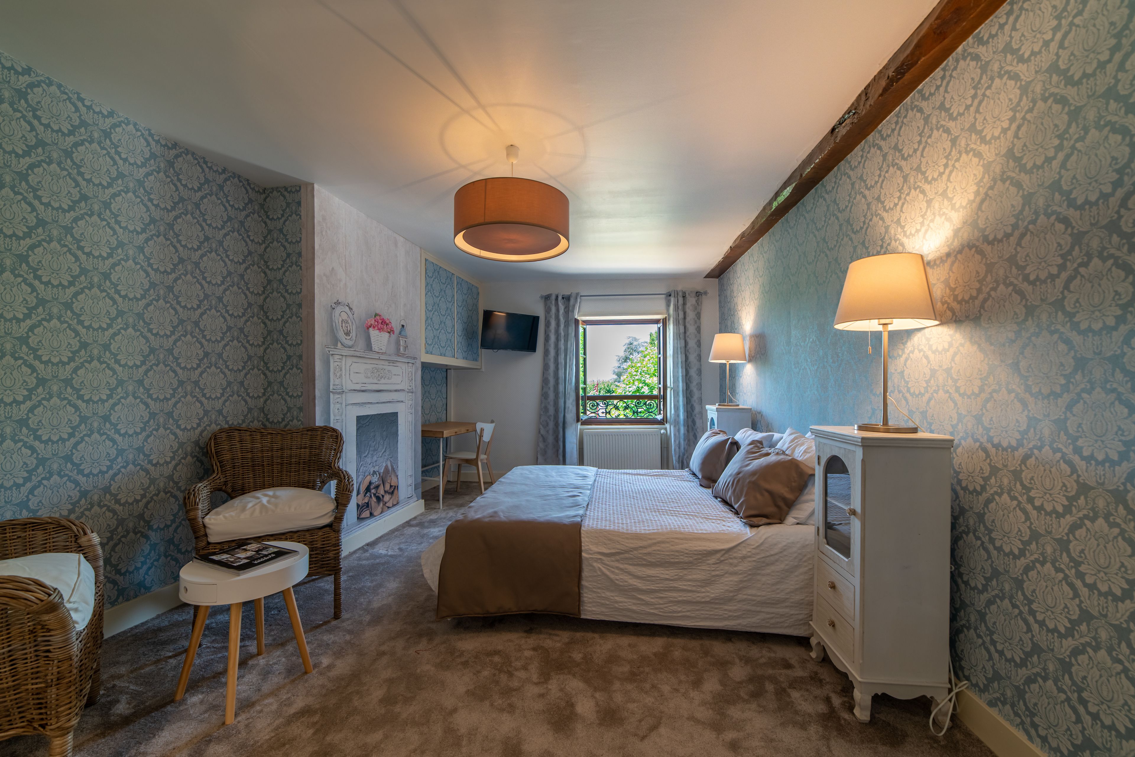 A bedroom with a bed, two chairs, a nightstand, a television, and a window with curtains.