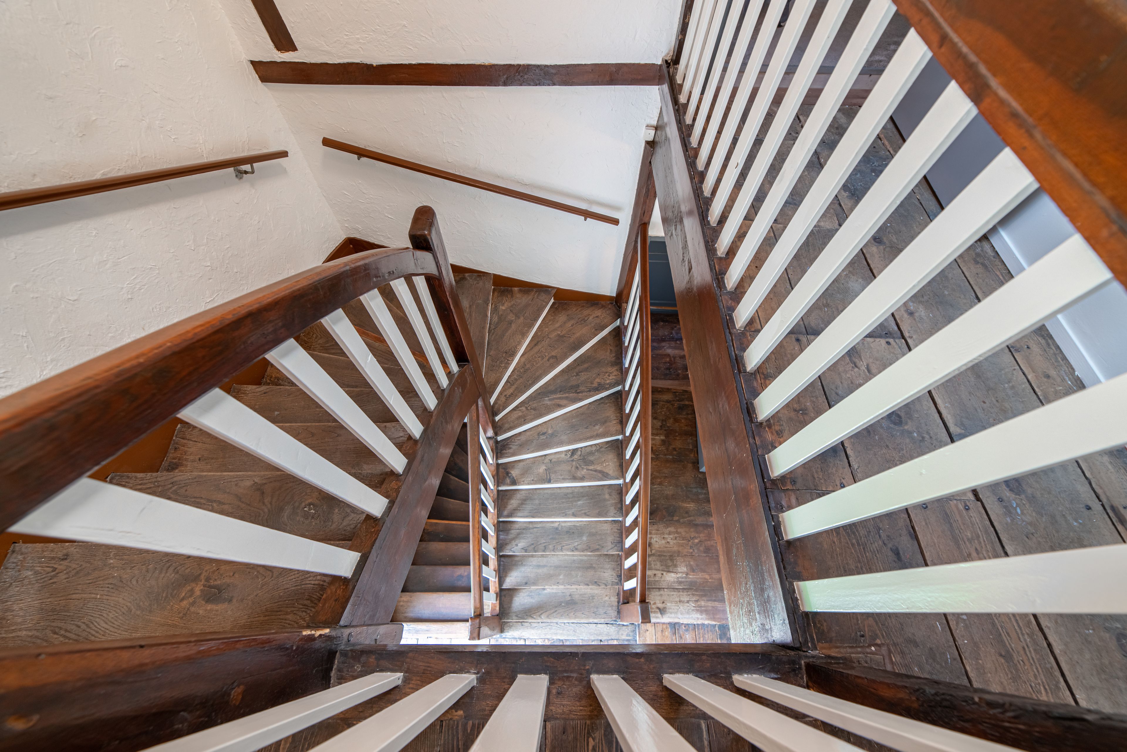A wooden spiral staircase with white balusters and a wooden handrail.