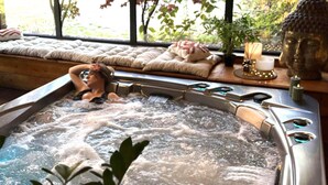A hot tub with a person relaxing, a cushioned bench, a Buddha statue, and a candle on a table.