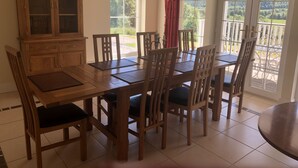 Ein Essbereich mit Holztisch und -stühlen, einem Schrank und großen Fenstern mit Blick ins Grüne.