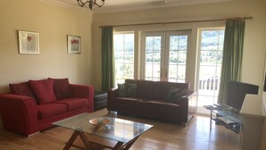 Ein Wohnzimmer mit zwei Sofas, einem Glastisch und einem Fernseher auf einem Schrank.