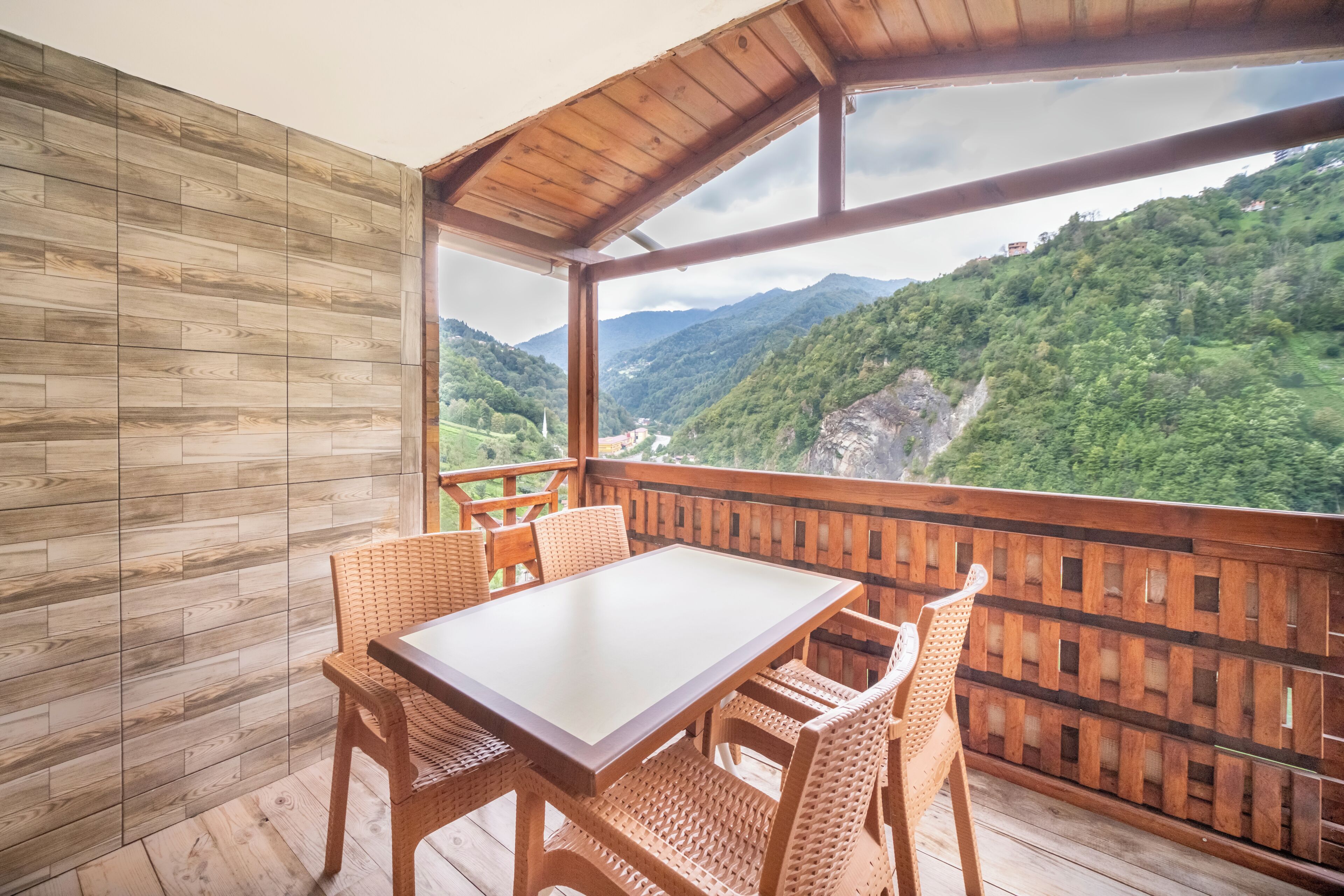 A wooden deck with a table and chairs, overlooking a mountainous landscape.