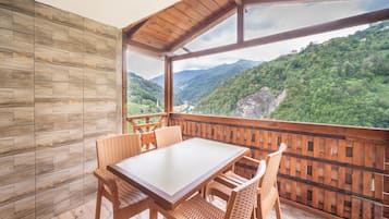 A wooden deck with a table and chairs, overlooking a mountainous landscape.