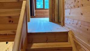 Een houten trap die leidt naar een kamer op de tweede verdieping, met een groot raam.