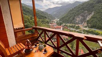 Une terrasse en bois avec une table dressée pour deux personnes, offrant une vue sur un paysage montagneux avec une route et des bâtiments.