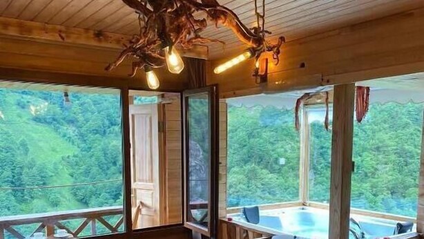 Een slaapkamer in een houten hutje, met een bed, een kroonluchter en uitzicht op het bos.