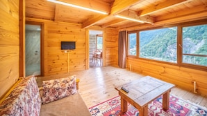 Interior de una cabaña de madera con sofá, mesa y televisor.