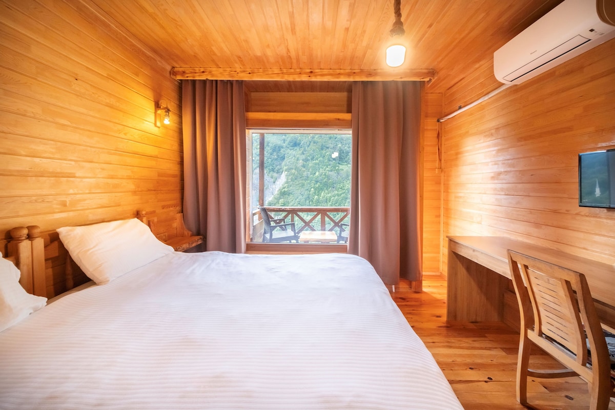 Een houten kamer met een bed, een bureau en een balkon met uitzicht op het bos.