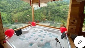 Una cabaña de madera con hidromasaje y vistas panorámicas de un valle boscoso.