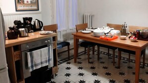 A kitchen with a stove, oven, and coffee maker. There is a dining table with chairs and a window with curtains. - Itinere Rooms - Hostel (Granada)