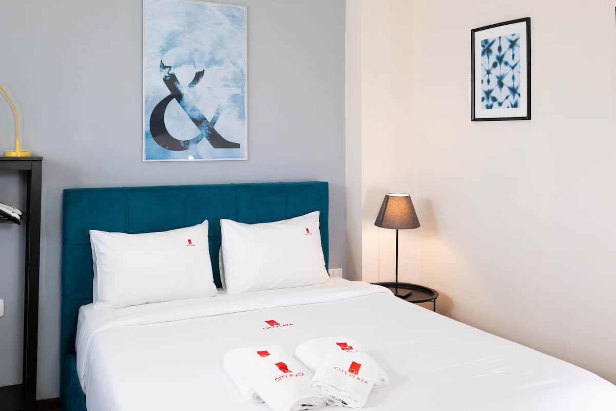 Een hotelkamer met een bed, hoofdeinde, nachtkastje, lamp en kunst aan de muren.