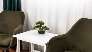 Une pièce avec deux fauteuils verts, une table blanche ornée d’une plante en pot et, au fond, un rideau blanc.