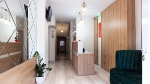 Un hall d’hôtel moderne avec un comptoir d’accueil en bois, un canapé vert et un couloir menant aux autres chambres.