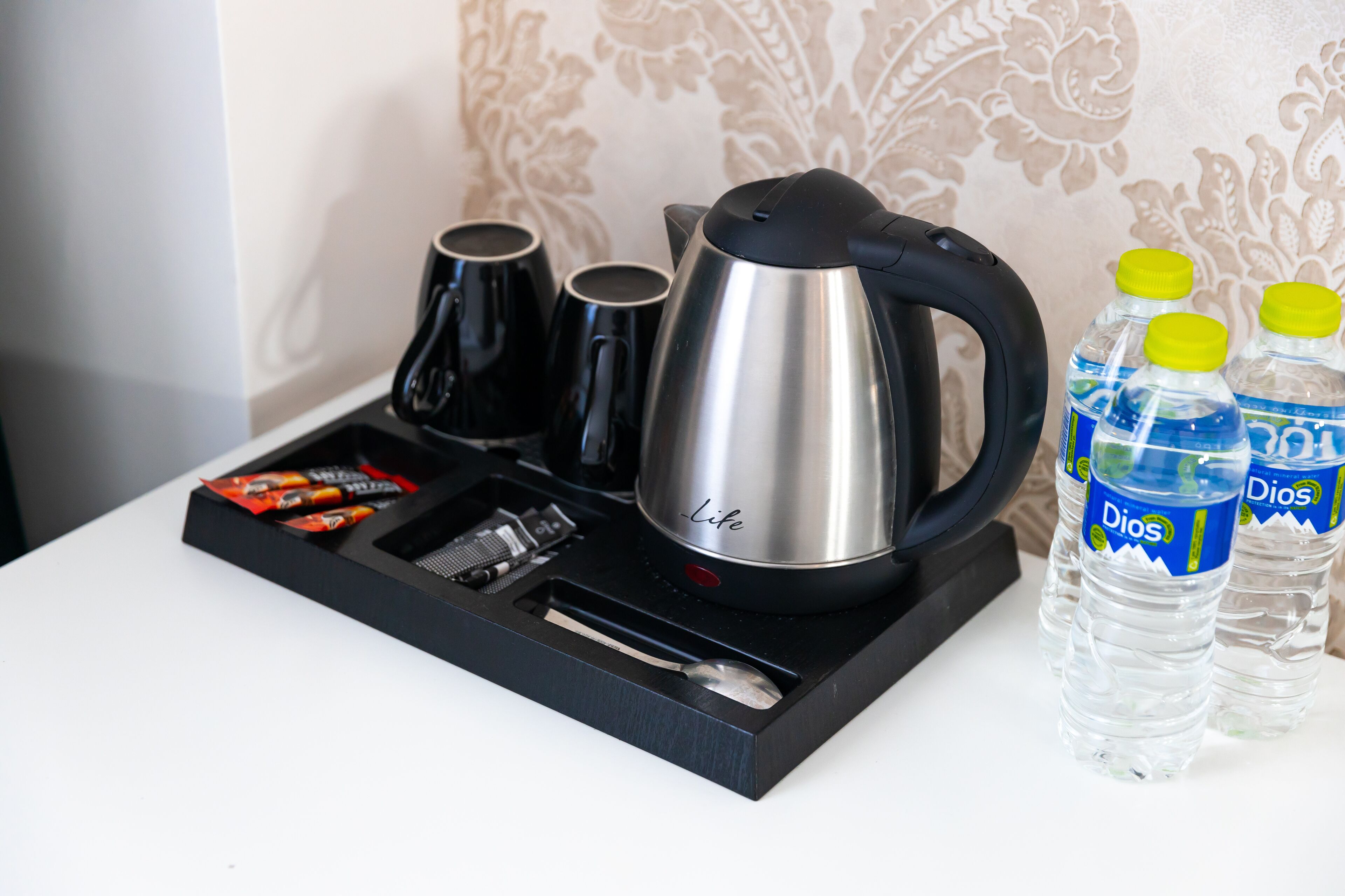 A coffee maker, two cups, a spoon, and two bottles of water on a tray.