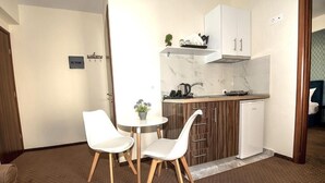 Une cuisine compacte avec des meubles blancs, un pare-feu en marbre, un petit coin repas avec deux chaises blanches et une seule plante en pot.