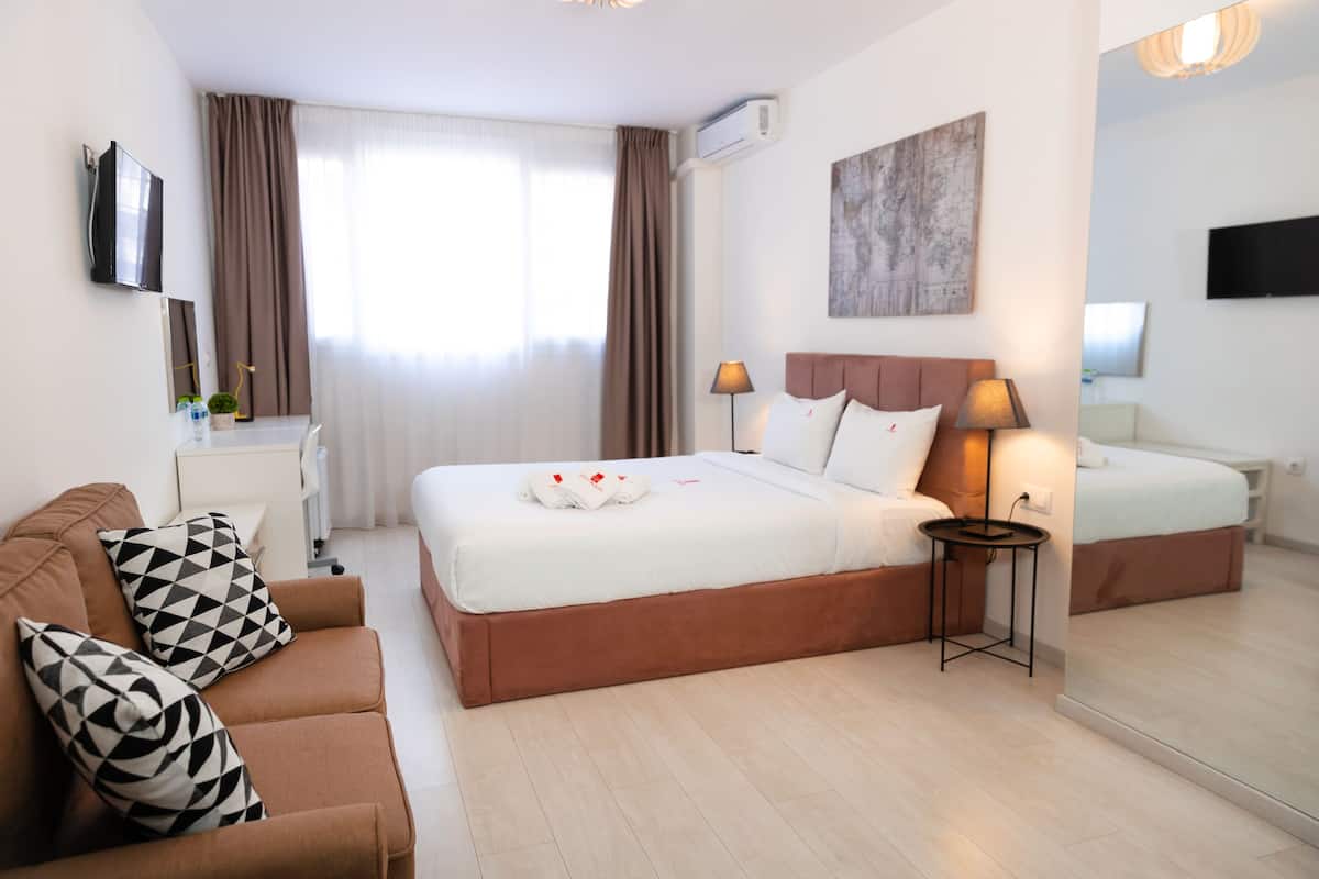 Een hotelkamer met een groot bed, een slaapbank, een nachtkastje, een lamp en een televisie.