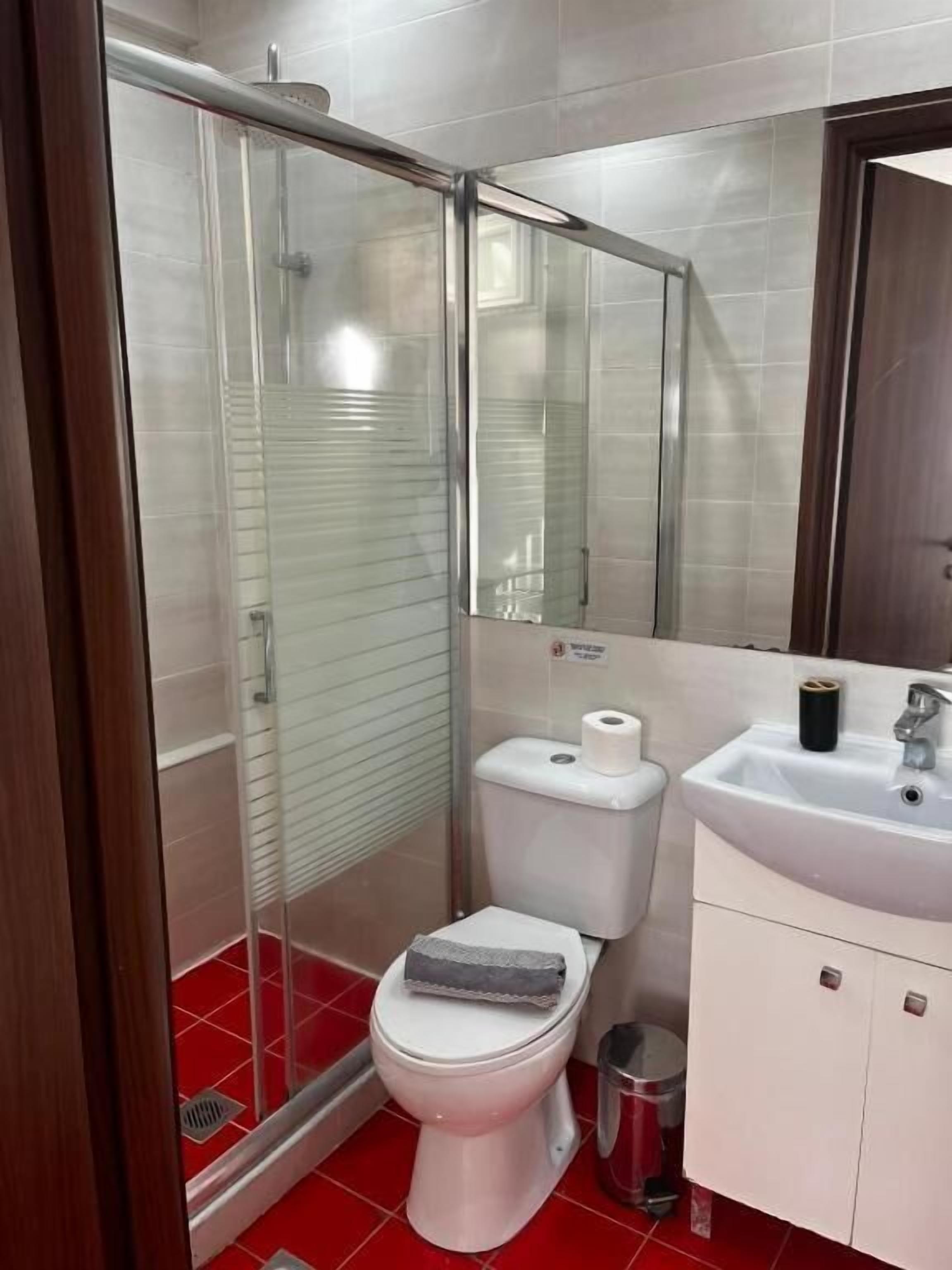 Un baño con cabina de ducha de vidrio, inodoro, lavamanos y espejo.