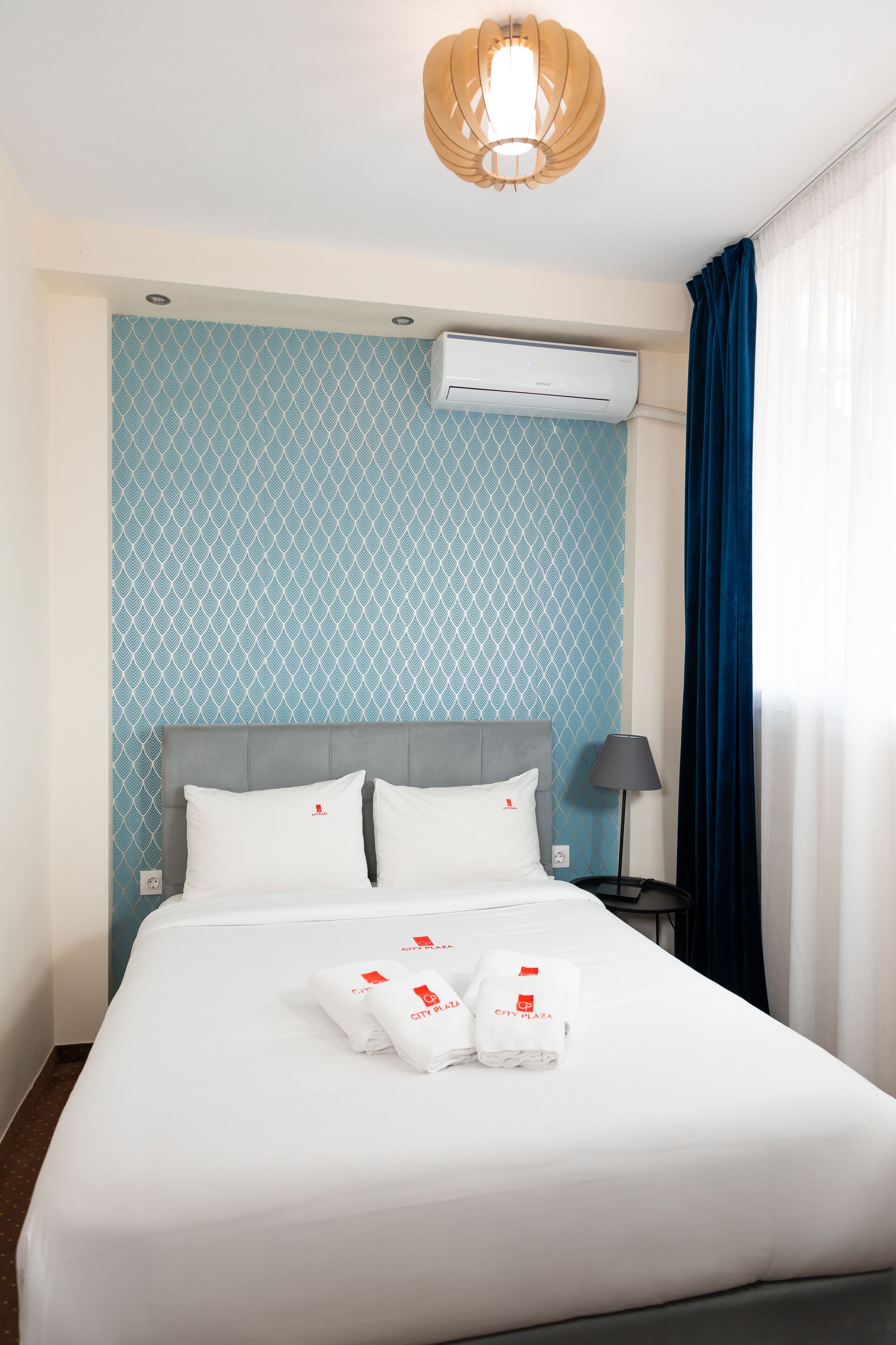 Een hotelkamer met een bed, nachtkastje, lamp en airconditioning.