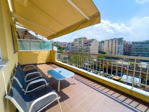 Een balkon met een geel zonnescherm, een tafeltje en twee stoelen.