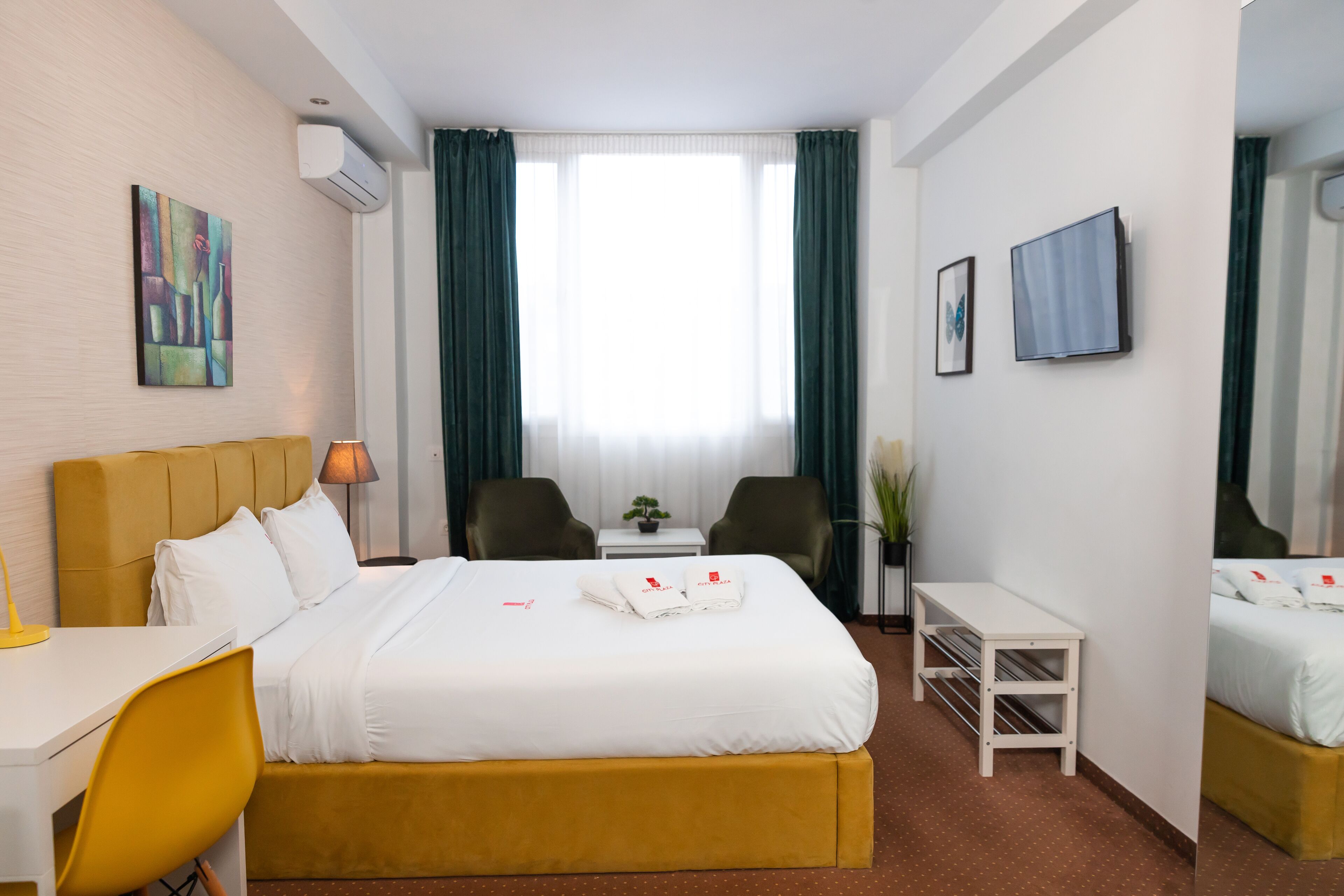 Une chambre d’hôtel équipée d’un lit, d’un bureau, d’une chaise, d’une télévision et d’une petite table sur laquelle est posée une plante.