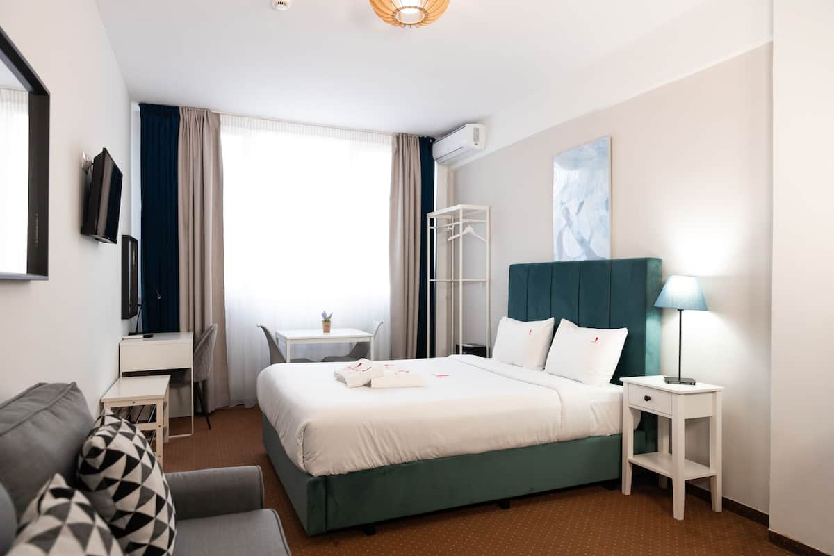 Een hotelkamer met een bed, een bureau, een stoel, een klein tafeltje, een televisie en een lamp.