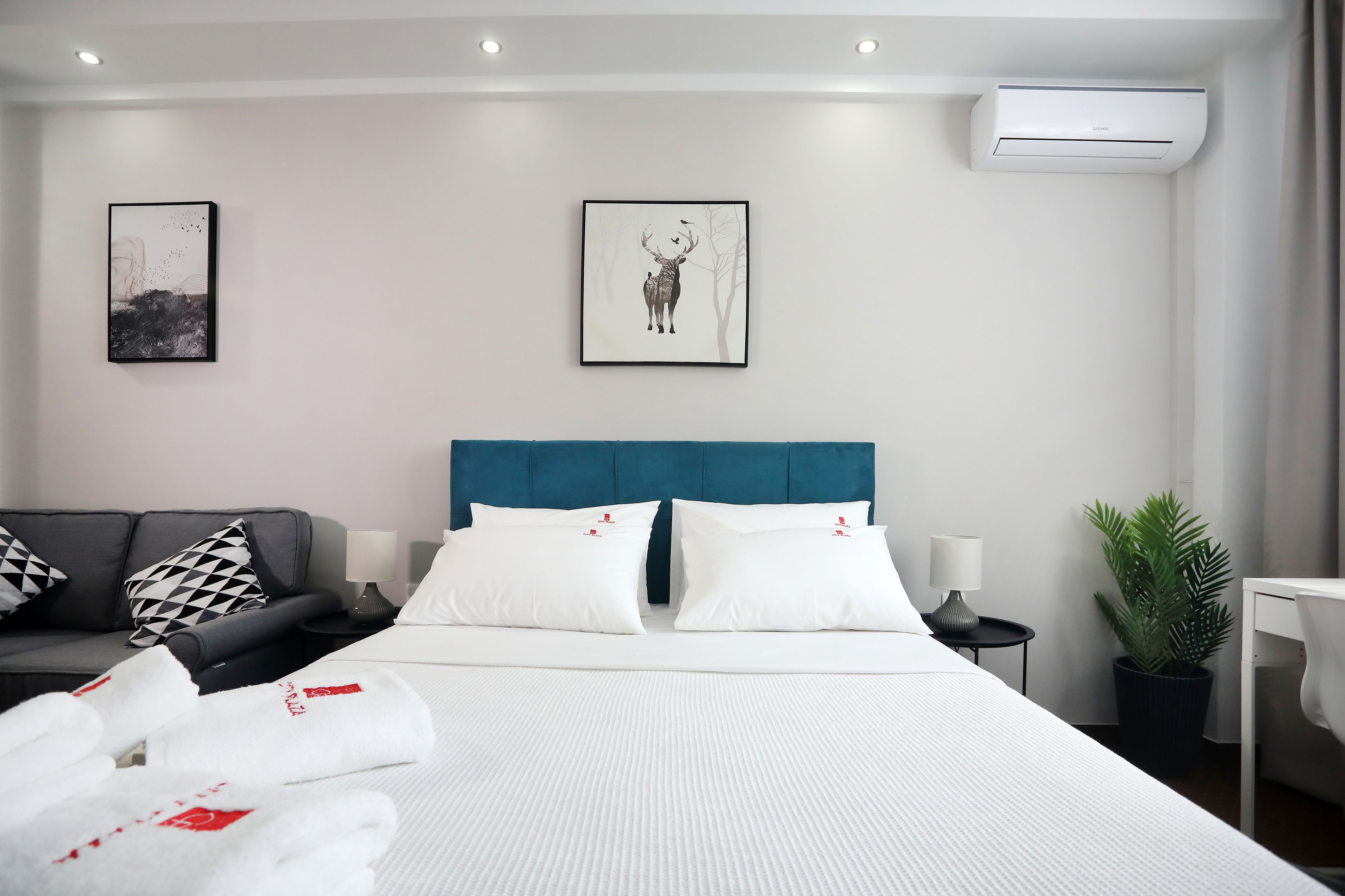 Una habitación de hotel moderna con una cama grande, un sofá, una mesita de noche, una lámpara y una planta en maceta.
