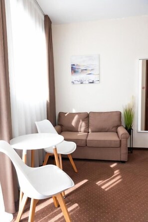 A room with a brown sofa, white chairs, a small table, a painting on the wall, and a plant. - City Plaza Apartments & Rooms (Thessaloniki)