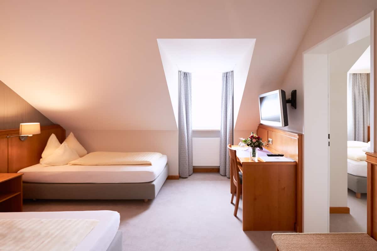 A hotel room with a bed, a desk, a chair, a TV, and a window with curtains.