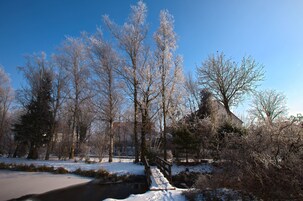 A snow-covered park with bare trees and a small bridge over a stream.