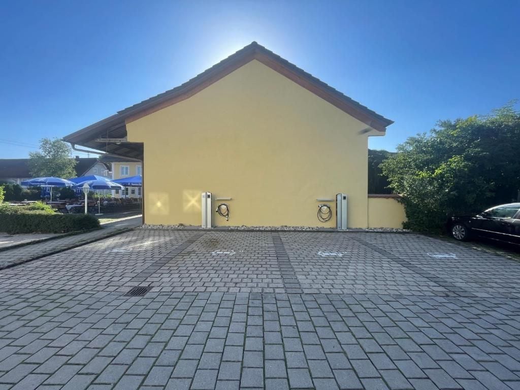 A building with a yellow facade, a sloped roof, and a paved entrance area.