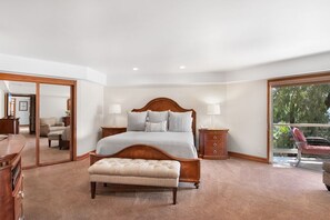 Un dormitorio amplio con una cama grande, un banco de madera, un aparador y un espejo.