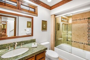 Baño con lavamanos de encimera de granito, inodoro y zona de ducha con mampara de vidrio.