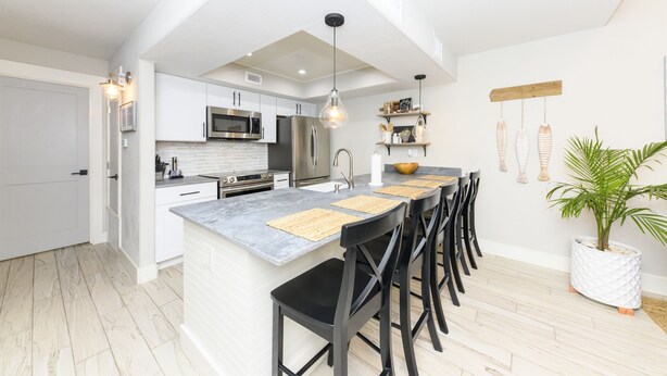 Een moderne keuken met witte kasten, een centraal eiland met barstoelen, roestvrijstalen apparatuur en hanglampen.