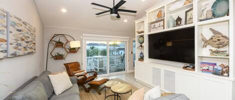A living room with a gray sofa, a wooden coffee table, a ceiling fan, and a TV on a white cabinet.