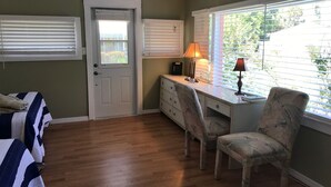 A bedroom with a bed, a desk with a chair, a dresser, and a window with blinds. - Mangrove Snapper Studio Cottage (Fort Pierce)