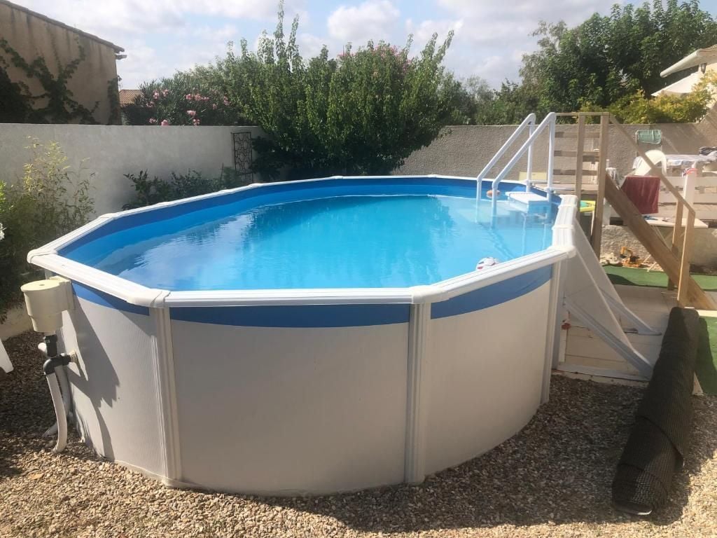 An above-ground swimming pool with a ladder, surrounded by gravel and vegetation.