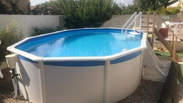 An above-ground swimming pool with a ladder, surrounded by gravel and vegetation.