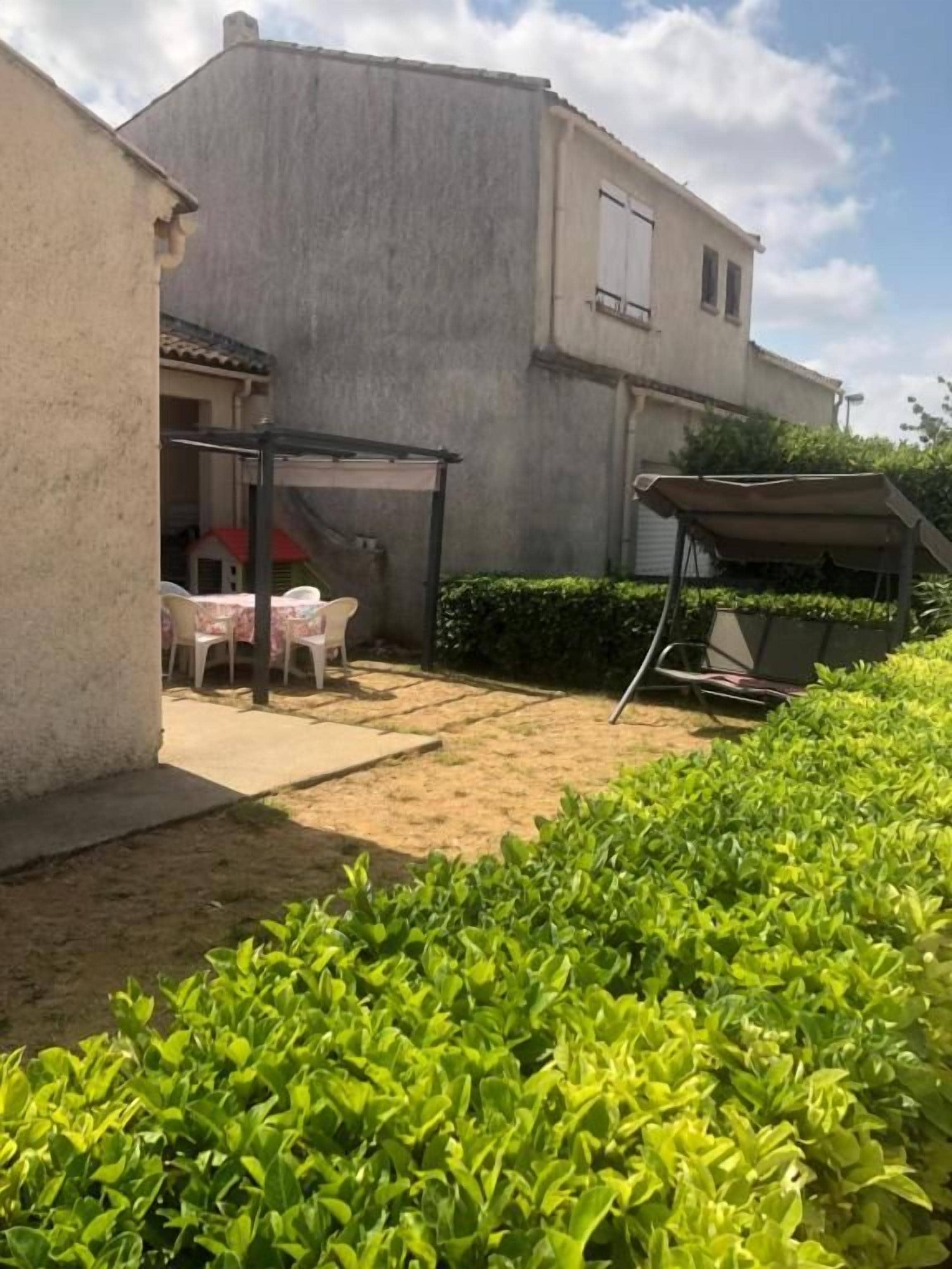 A residential property with a patio area, a covered seating area, and a well-maintained hedge.