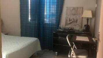 A bedroom with a bed, desk, chair, and curtains.