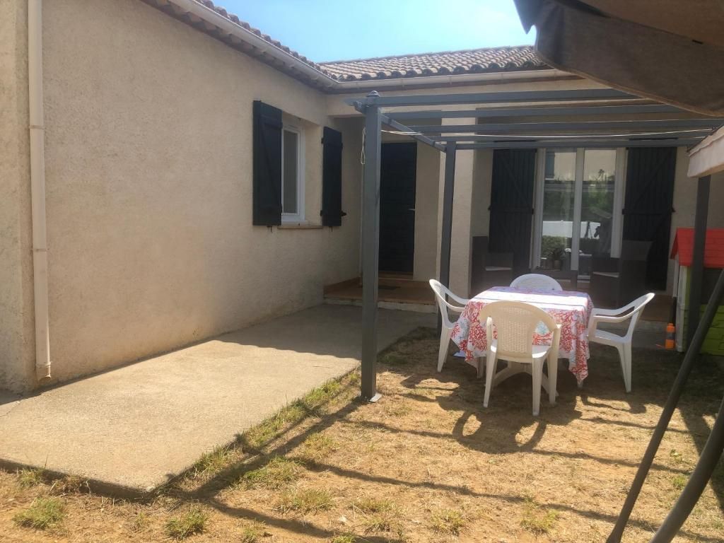 Una veranda riparata all'aperto con tavolo e sedie, una pavimentazione in cemento e un edificio con finestre.