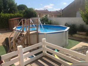 A backyard with a swimming pool, wooden deck, and a white fence. - Les Amandiers (Abeilhan)