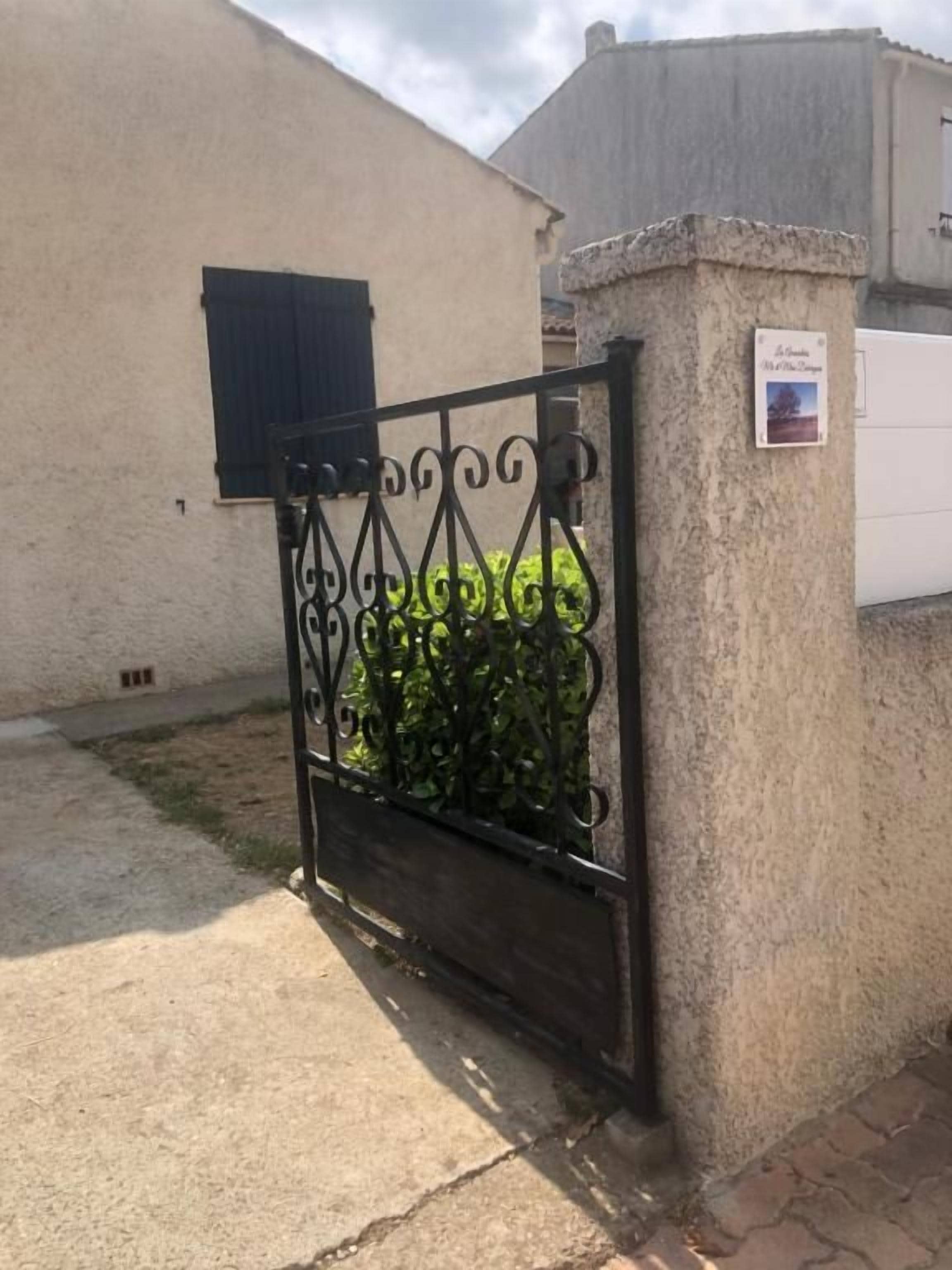 Una entrada vigilada con un portón metálico, un pilar de concreto y un pequeño letrero en el pilar.
