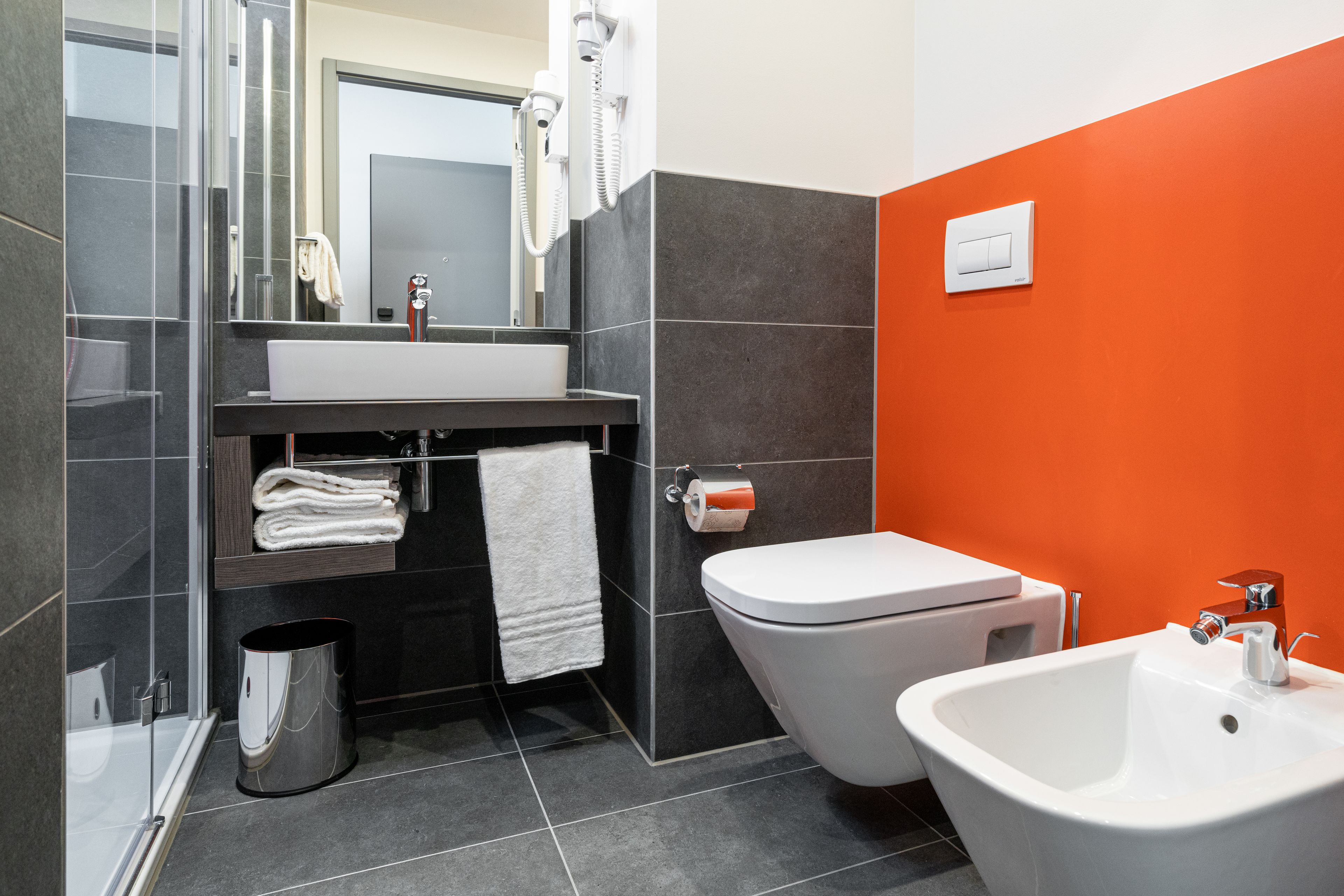 Un baño moderno con cabina de ducha de vidrio, un lavabo blanco, un inodoro y un bidé.
