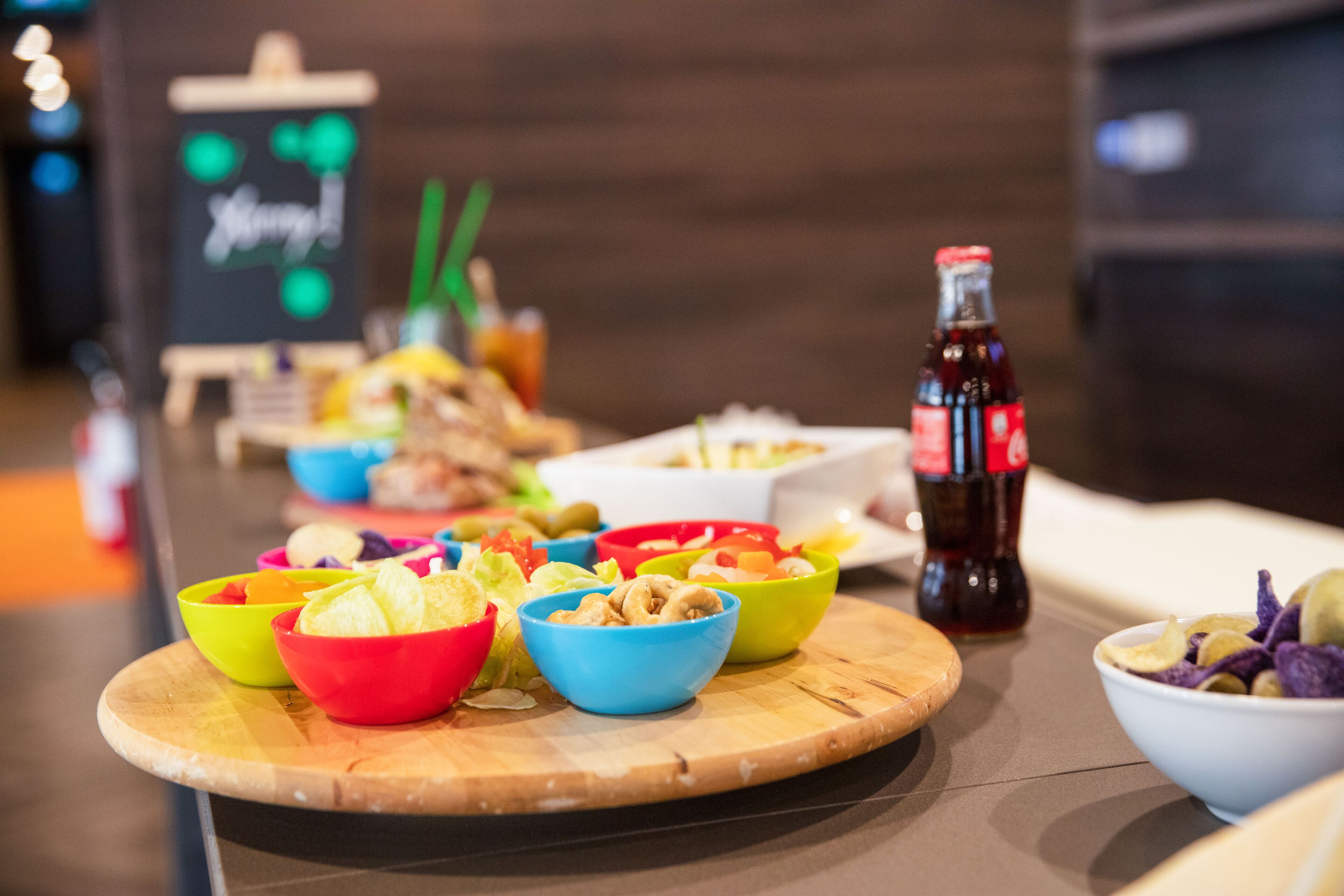 Una mesa con varios cuencos de colores llenos de aperitivos y una botella de refresco.