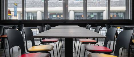 A restaurant with a long table and multiple chairs, large windows with a view of buildings outside.