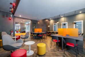Un espace repas moderne avec des tables rondes, des chaises grises et rouges, et des tabourets jaunes.