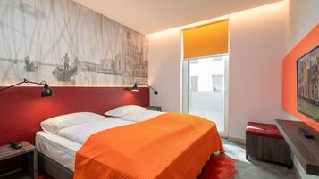 A modern hotel room with a bed, a desk, a chair, and a large window.