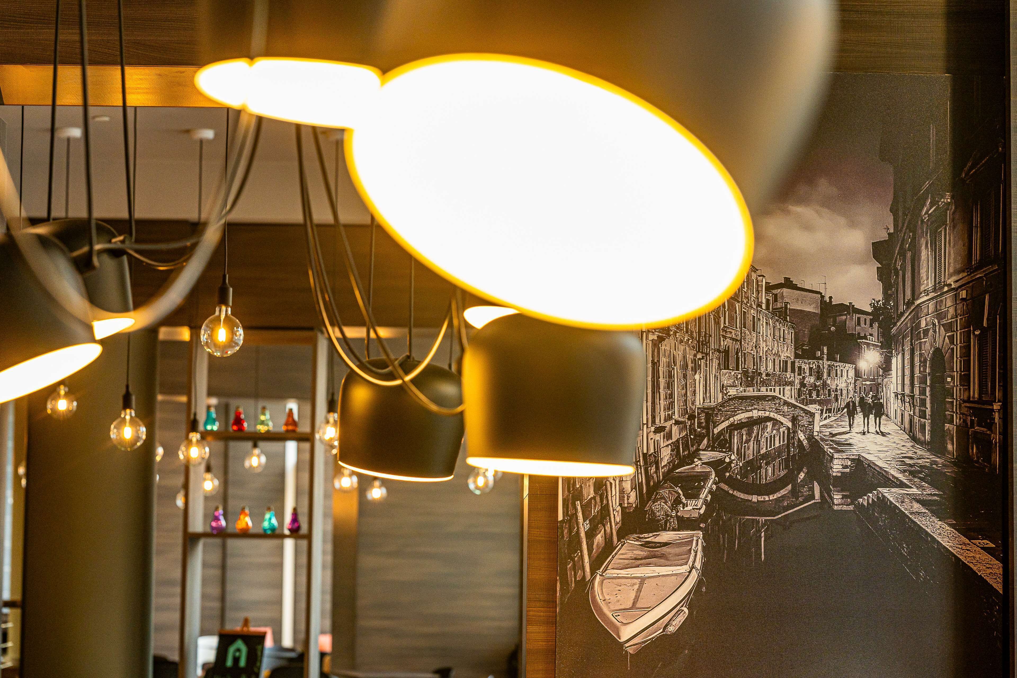 A room with hanging pendant lights, a wall-mounted shelf with colorful bottles, and a mural of a canal scene.
