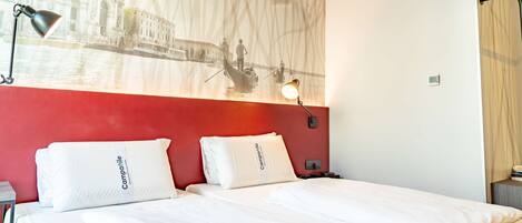 A hotel room with two beds, a red accent wall, a mural of a canal scene, and a nightstand with a lamp.