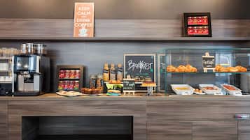 Zona de petit esmorzar amb una màquina de cafè, pots de condiments i varietat de pastissos i productes de forneria.